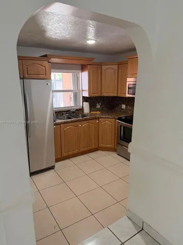 Kitchen featuring arched entryway, natural wood-finish cabinetry, stainless steel appliances, stone-finish countertops, and ceramic tile flooring