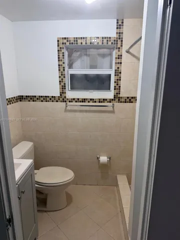 Bathroom featuring large-format wall tiling with decorative mosaic trim, tile flooring, built-in vanity cabinet, and a window with integrated tiling surround