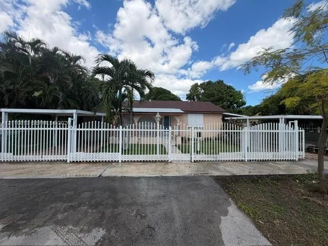 Single-story residence featuring a white metal perimeter fence, dual covered carports, and arched entryway detailing