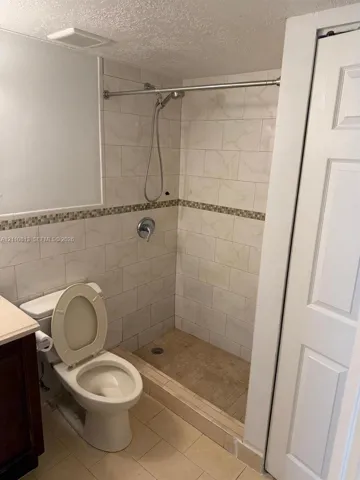 Walk-in shower with tiled walls, decorative mosaic accent tile, and a handheld shower head, complemented by tile flooring and a dual-panel interior door