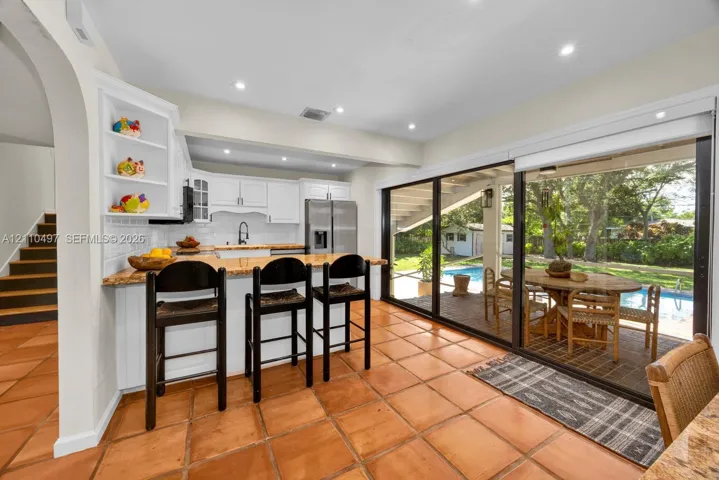 Kitchen featuring white cabinetry, stone countertops, stainless steel appliances, ceramic tile flooring, and large sliding glass doors