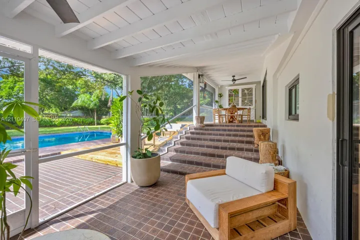 Screened-in patio featuring a vaulted ceiling with exposed rafters, dark tiled flooring, and a multi-level masonry staircase leading to the exterior pool area