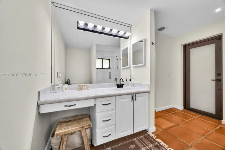 Bathroom vanity featuring white cabinetry, stone-composite countertop, integrated sink, matte black faucet, and full-width wall mirror with integrated lighting