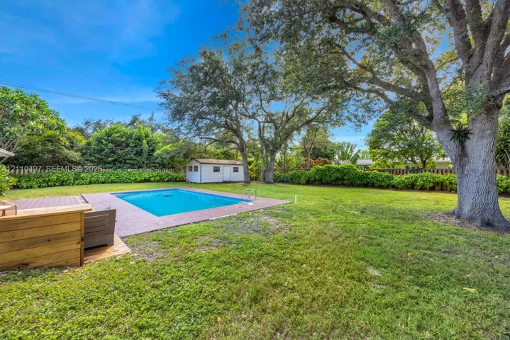 Spacious backyard featuring an in-ground swimming pool, brick paver decking, mature oak trees, and a detached storage structure