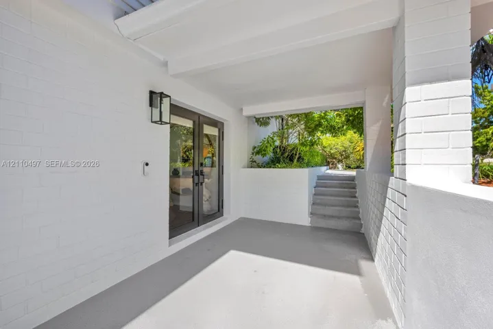 Covered entrance featuring white painted brick masonry, double glass-panel entry doors, concrete flooring, and an attached rectangular wall-mounted lantern