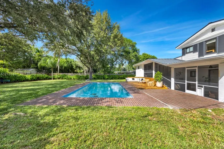 Rear exterior featuring a rectangular in-ground pool, brick paver patio, screened-in enclosure, and mature trees on a lawn