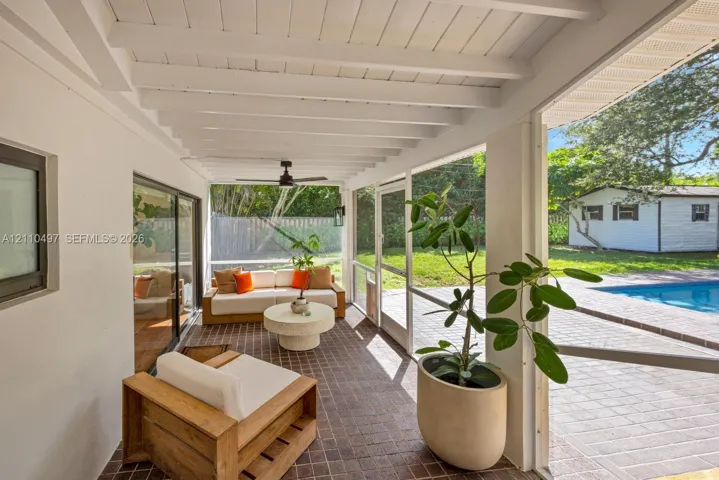 Screened-in patio featuring a vaulted ceiling with exposed beams, ceiling fan, dark tile flooring, and direct exterior access to a paved pool deck