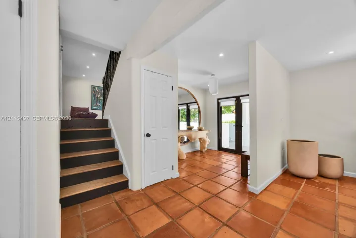 Interior entry featuring square terra-cotta tile flooring, staircase with dark-finished risers and wood treads, recessed ceiling lighting, and glass-paneled exterior door