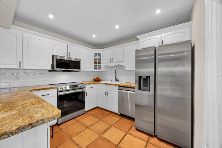 Kitchen featuring white cabinetry, stone countertops, stainless steel appliances, white subway tile backsplash, and terracotta-style flooring