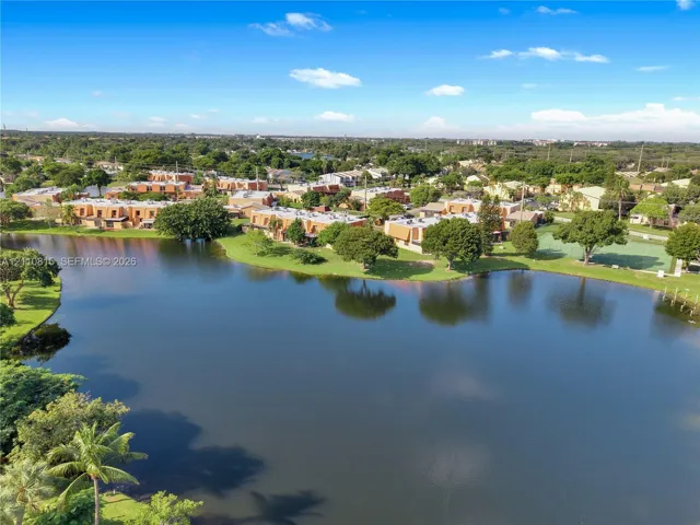 Aerial perspective of waterfront property featuring expansive lake frontage, mature trees, and an outdoor recreational court
