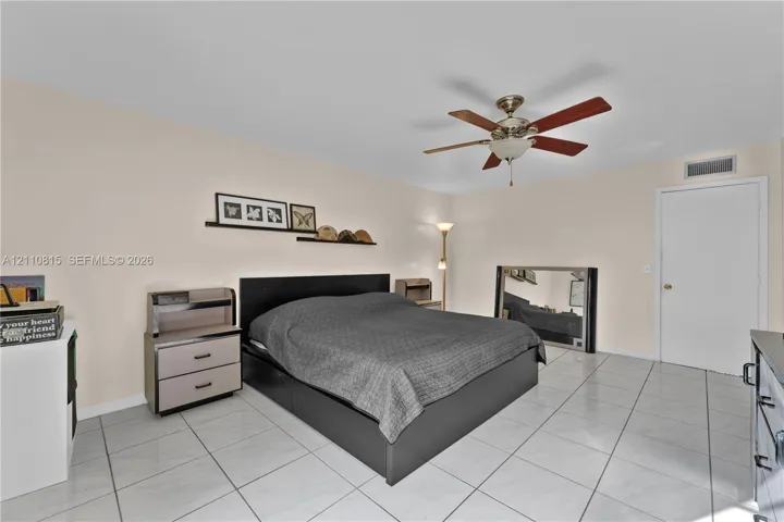 Neutral-toned room featuring large-format ceramic tile flooring, a centered ceiling fan with integrated lighting, and a white interior door