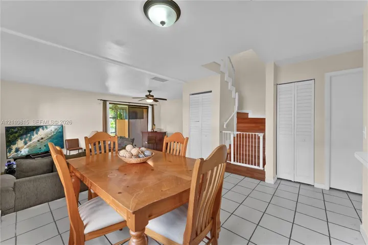 Interior area featuring white tile flooring, staircase with wood-finish treads, ceiling fan with light fixture, and dual-closet storage with louvered doors