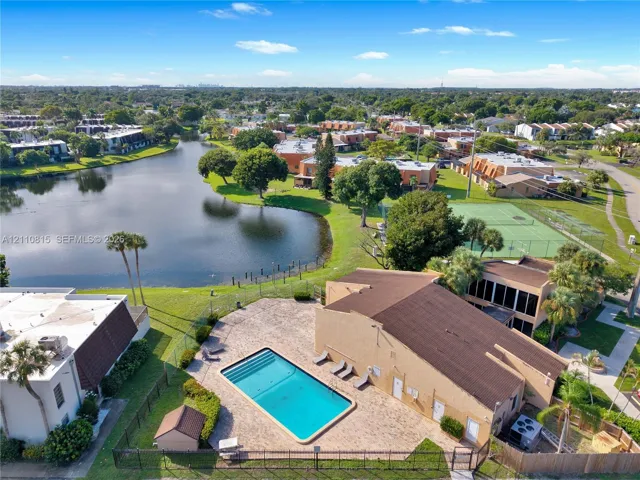 Aerial perspective of a community featuring a swimming pool with paver decking, a tennis court, a pond, and mature landscaping