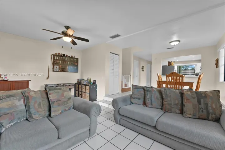 Living area featuring light-toned tile flooring, recessed lighting, a ceiling fan, and a pass-through opening to a dining space