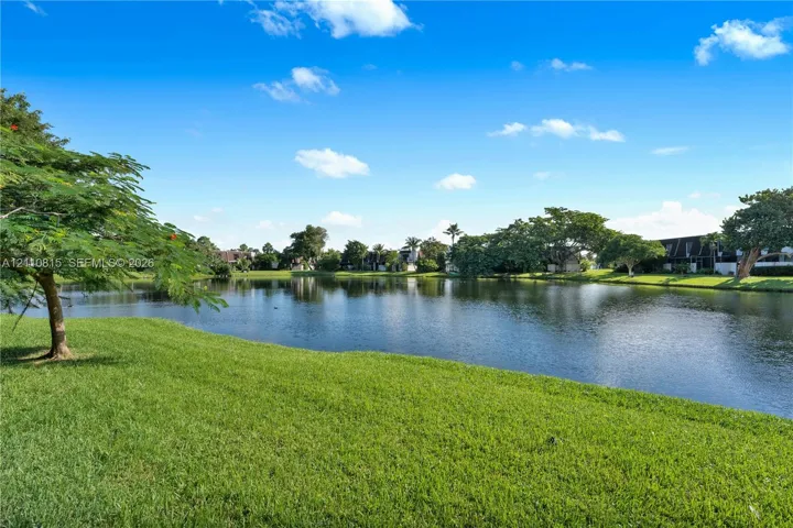 Waterfront setting featuring a grass lawn, mature trees, and landscaping