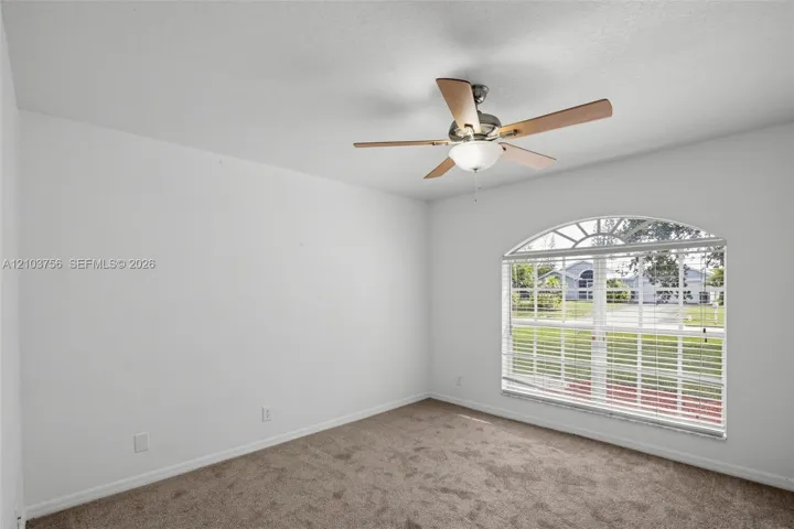 Room featuring neutral wall-to-wall carpeting, an arched window, and a multi-blade ceiling fan with an integrated light fixture