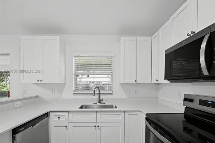 Kitchen featuring white shaker-style cabinetry, solid-surface countertops, undermount stainless steel sink with high-arc faucet, and stainless steel appliances
