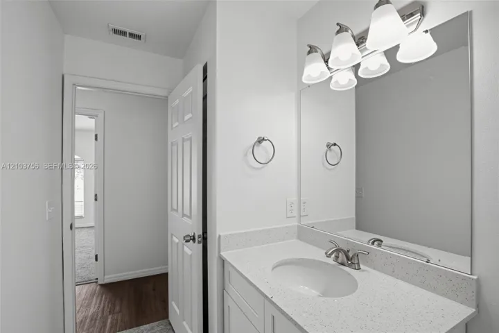 Bathroom vanity featuring a speckled white countertop, oval undermount sink, multi-light fixture, large wall-mounted mirror, and metal ring towel holder