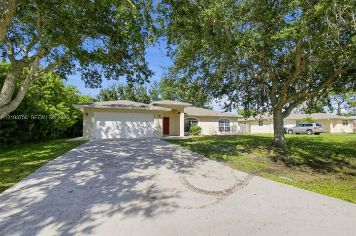 Single-story residence featuring a stucco exterior, an attached two-car garage, arched windows, and mature trees on a lot with lawn space