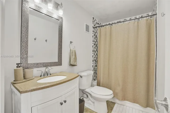 Bathroom featuring a white vanity cabinet, solid-surface countertop with an integrated basin, mosaic-tiled mirror frame, three-light fixture, and a tile-surround shower area