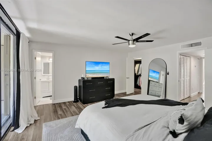 Neutral-toned wood-finish flooring, brushed metal ceiling fan, and louvered closet doors