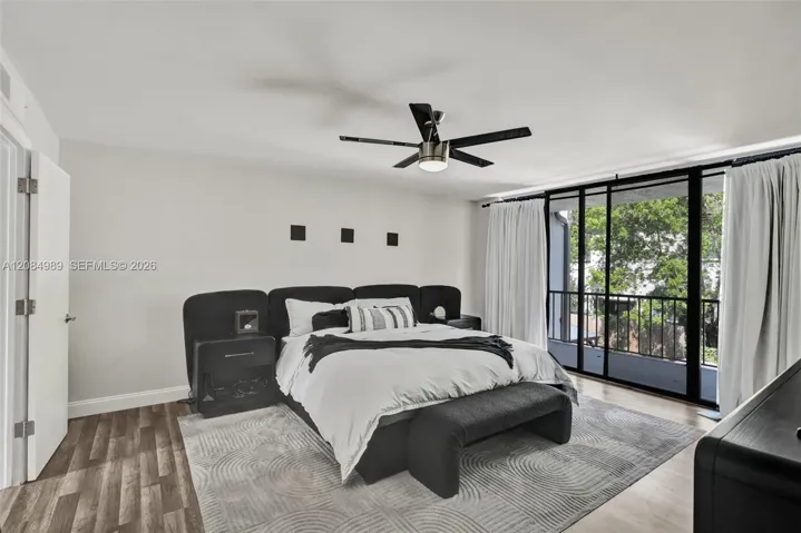 Room featuring wood-finish flooring, a matte black multi-blade ceiling fan with integrated lighting, and floor-to-ceiling sliding glass doors opening to a private balcony