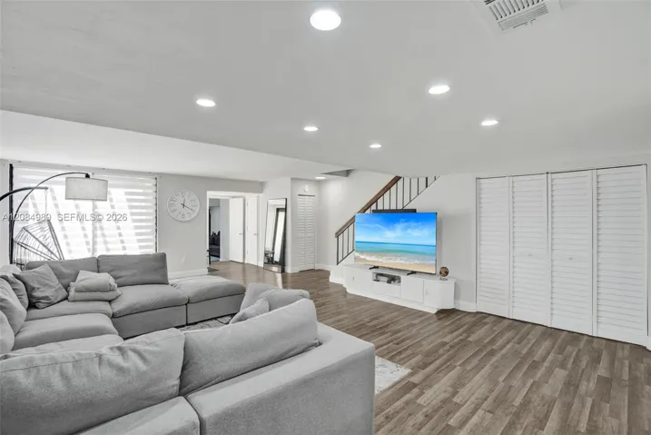 Living area featuring wood-finish flooring, recessed lighting, multi-panel louvered closet doors, and a staircase with a wooden handrail and metal balusters