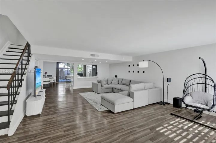 Open-concept living space featuring wood-finish flooring, recessed lighting, and a staircase with a metal railing and wood handrail