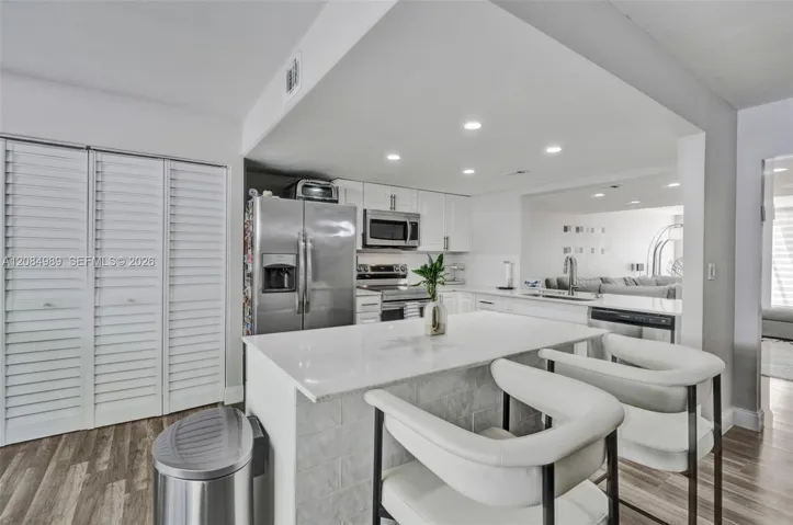 Kitchen featuring a stone-surface island, stainless steel appliances, white cabinetry, recessed lighting, and wood-finish flooring