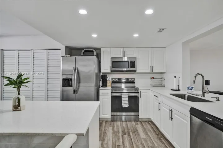 Kitchen featuring white shaker-style cabinetry, solid-surface countertops, recessed lighting, wood-finish flooring, and stainless steel appliances