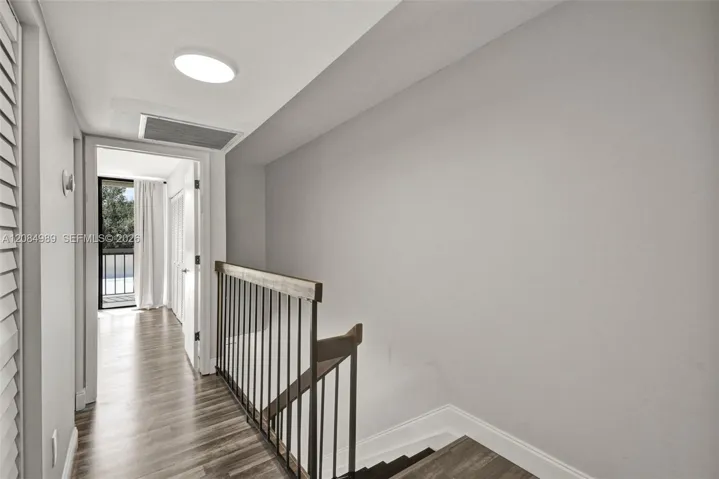 Wood-finish flooring, staircase featuring a dark-toned handrail, and metal balusters