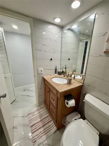 Full-height wall tiling featuring stone-patterned surfacing, vanity with integrated stone countertop and oval undermount sink, wall-spanning vanity mirror, recessed ceiling lighting, and large-format floor tiling
