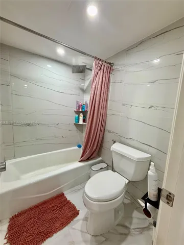 Full-height wall tiling featuring veined detailing, white acrylic bathtub, integrated shower head, recessed ceiling lighting, and large-format tile flooring