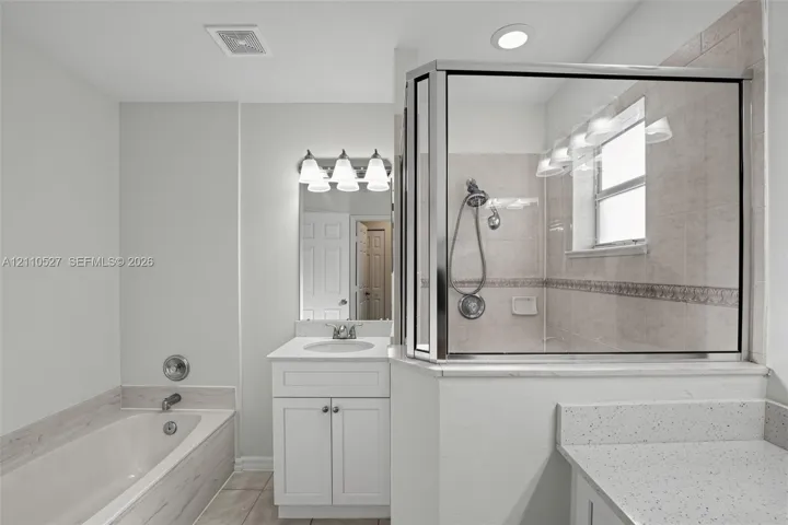 Bathroom featuring a glass-enclosed shower with tiled walls, a deep soaking tub with a tiled surround, white shaker-style cabinetry, and light-toned solid surface countertops
