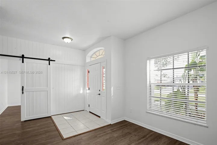 Entryway featuring vertical white wood-paneling, a sliding barn door, ceramic tile flooring, wood-finish flooring, and an arched transom window above the front door