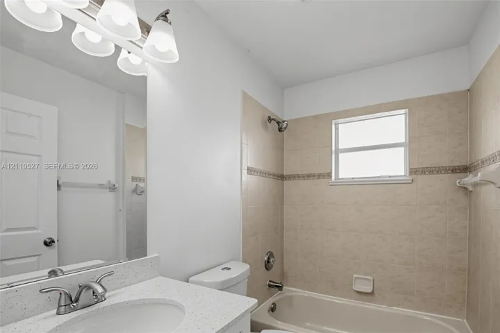 Bathroom featuring a speckled countertop with an integrated basin, multi-bulb vanity light, polished chrome hardware, and neutral tile surround with a decorative border accent