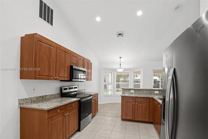 Kitchen featuring wood cabinetry, stone countertops, stainless steel appliances, tile flooring, and a vaulted ceiling