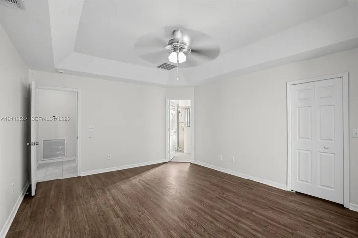 Tray ceiling featuring a central brushed-metal ceiling fan, wood-finish flooring, and white two-panel closet doors