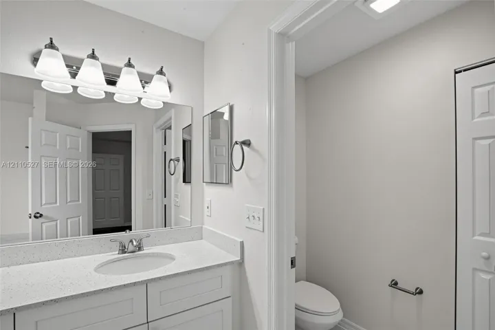 Bathroom vanity featuring an integrated oval sink, stone-composite countertop, shaker-style cabinetry, a wall-to-wall mirror, and a four-light fixture
