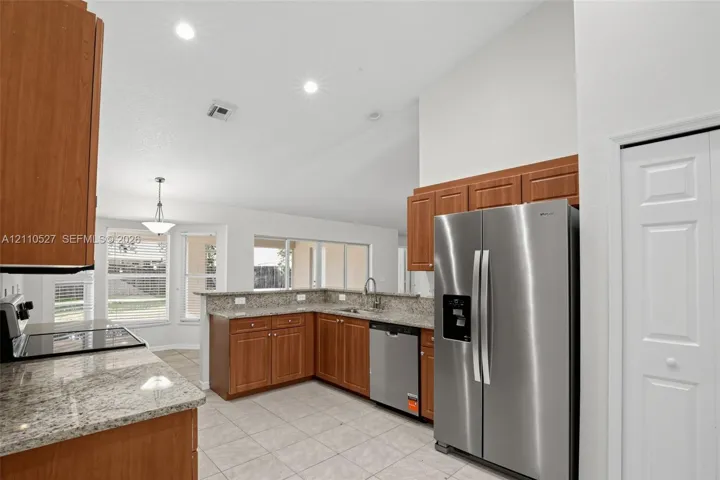 Kitchen featuring wood cabinetry, stone-finish countertops, stainless steel appliances, tile flooring, and vaulted ceilings