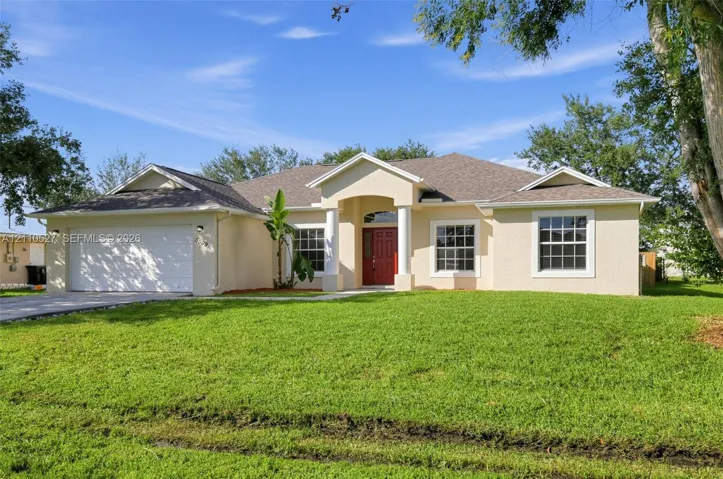 Stucco exterior residence featuring an arched entry with columns, a multi-gabled roofline, a two-car garage, and grid-pattern windows