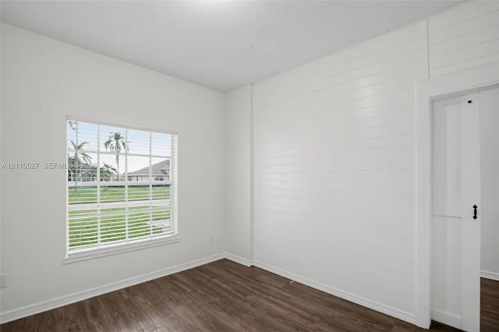 Interior space featuring wood-finish flooring, horizontal shiplap wall accent, multi-pane window with white blinds, and a white sliding door with black hardware