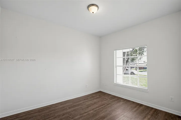 Room featuring neutral-toned walls, wood-finish flooring, a multi-pane window with integrated blinds, and a dome-style flush-mount ceiling light