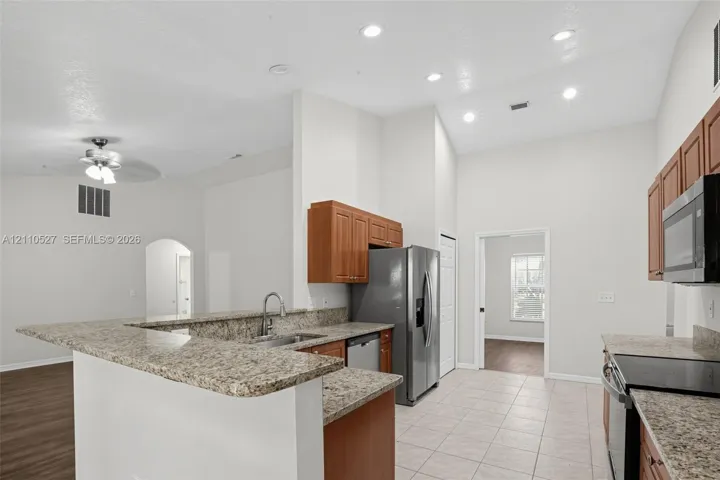 Kitchen featuring stone-finish countertops, stainless steel appliances, wood cabinetry, recessed lighting, and tile flooring