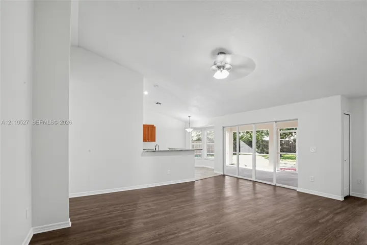 Open living area featuring vaulted ceilings, wood-finish flooring, a ceiling fan, and sliding glass doors with exterior access