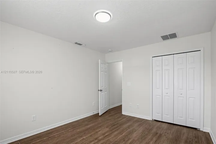 Room with neutral wall color, wood-finish flooring, white paneled interior door, and white bi-fold closet doors