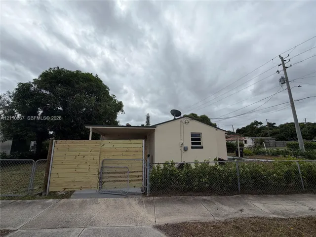 Stucco exterior with a covered side porch, horizontal wood-slat privacy fencing, and chain-link perimeter fencing