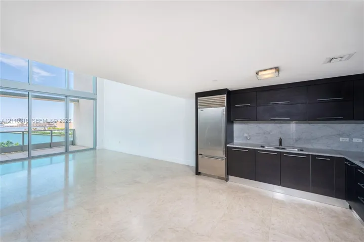 Kitchen featuring dark cabinetry, integrated stainless steel refrigerator, stone-style backsplash, and light-toned flooring, with floor-to-ceiling windows