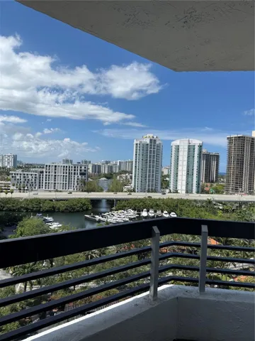 Private balcony featuring a black metal railing overlooking a waterway, boat slips, and an urban cityscape