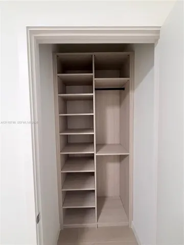 Built-in closet featuring light wood-finish shelving, multiple open storage compartments, and a horizontal hanging rod